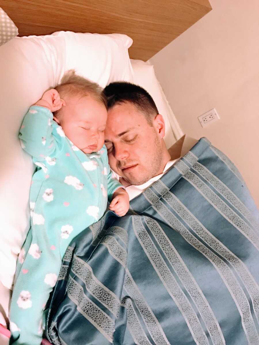 Dad sleeps in bed with newborn baby with a striped blanket