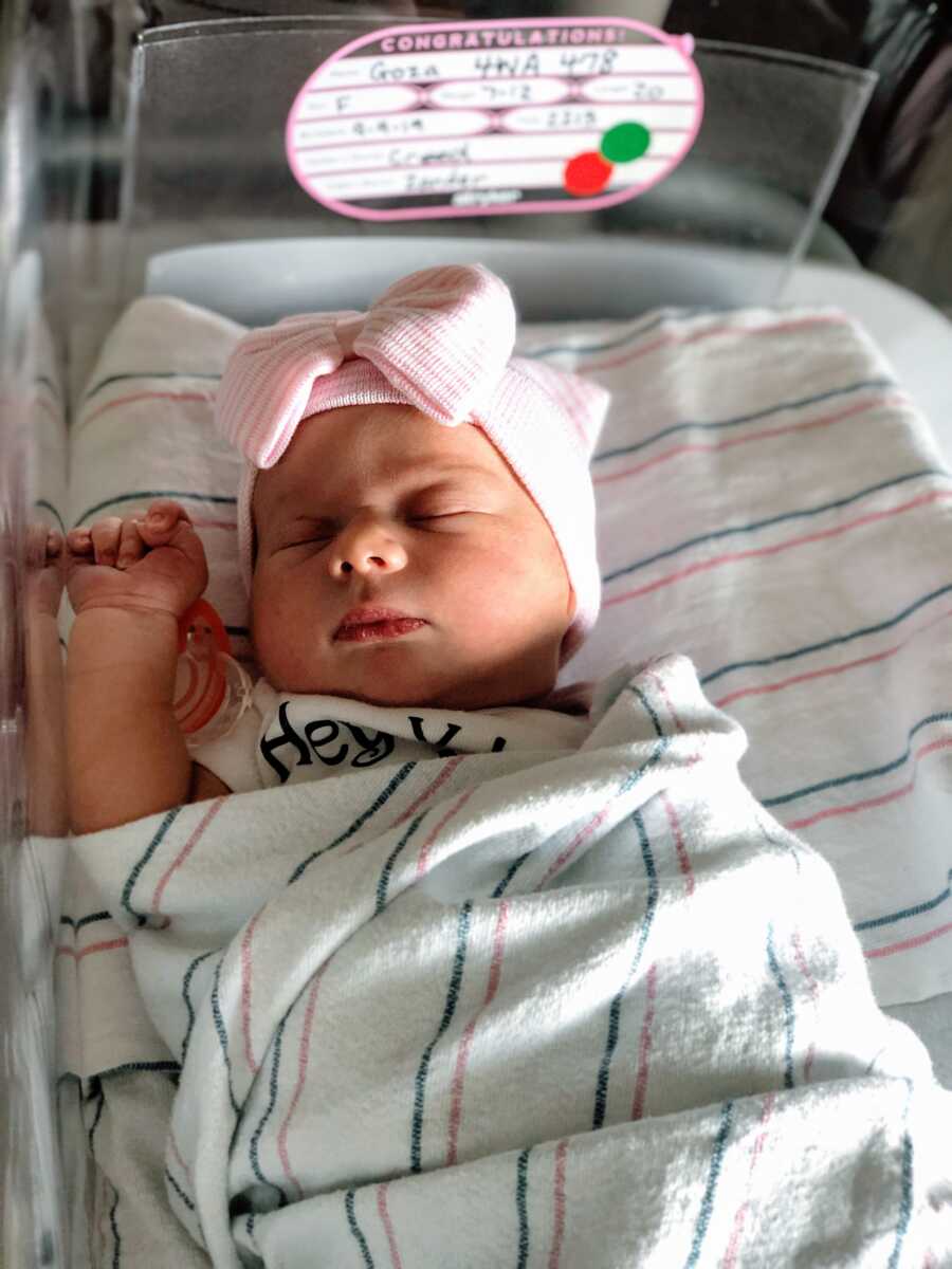 Newborn baby sleeps in hospital cot with a pink bow on her head