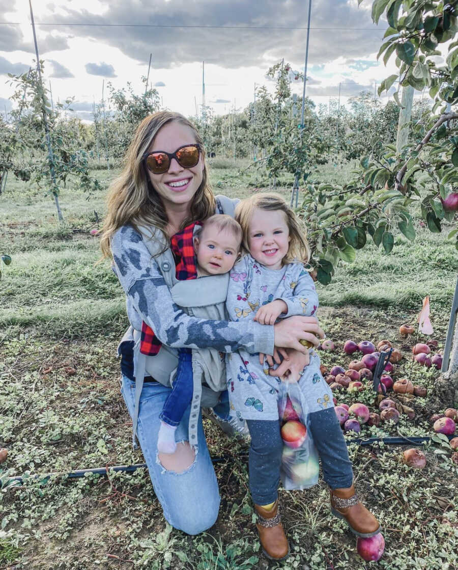 Mom hugging her two kids, a boy and a girl, while picking apples outdoors