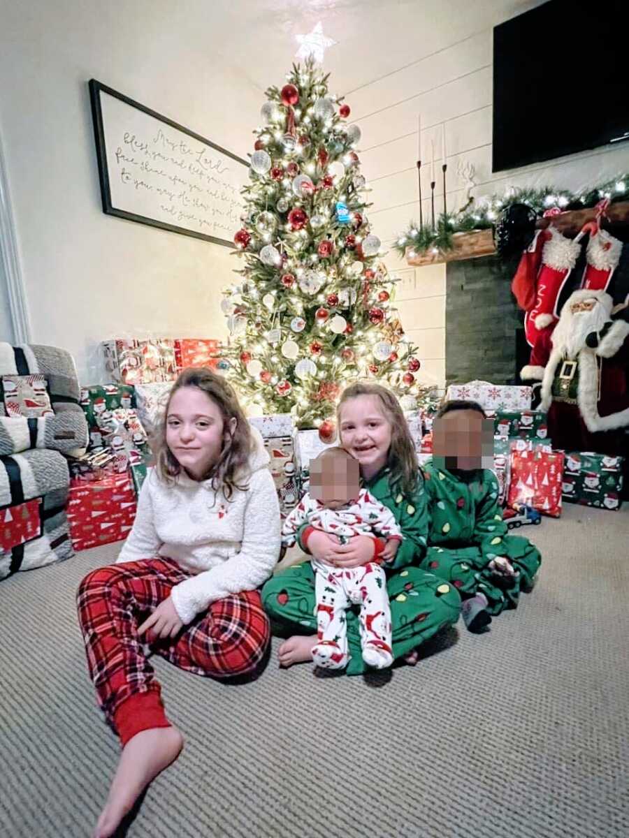 Mom takes photo of her two biological children and two foster children all sitting together in front of the Christmas tree