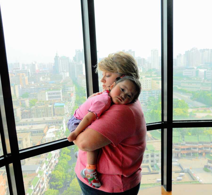 Single teacher comforts scared toddler being adopted from China. 