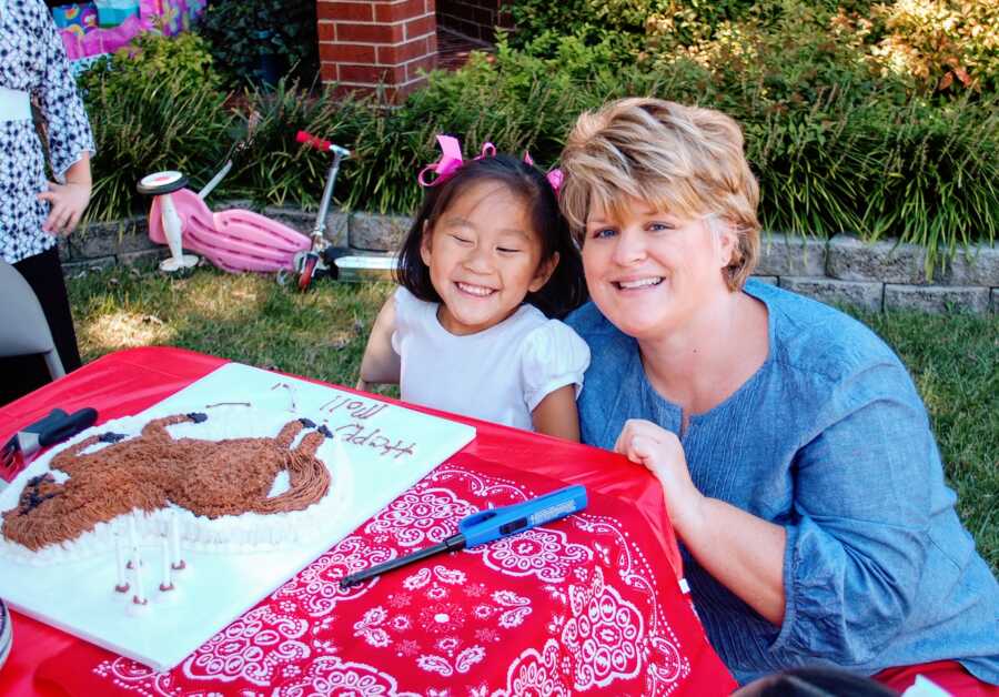 Single adoptive mom and daughter take picture next to horse-shaped birthday cake.