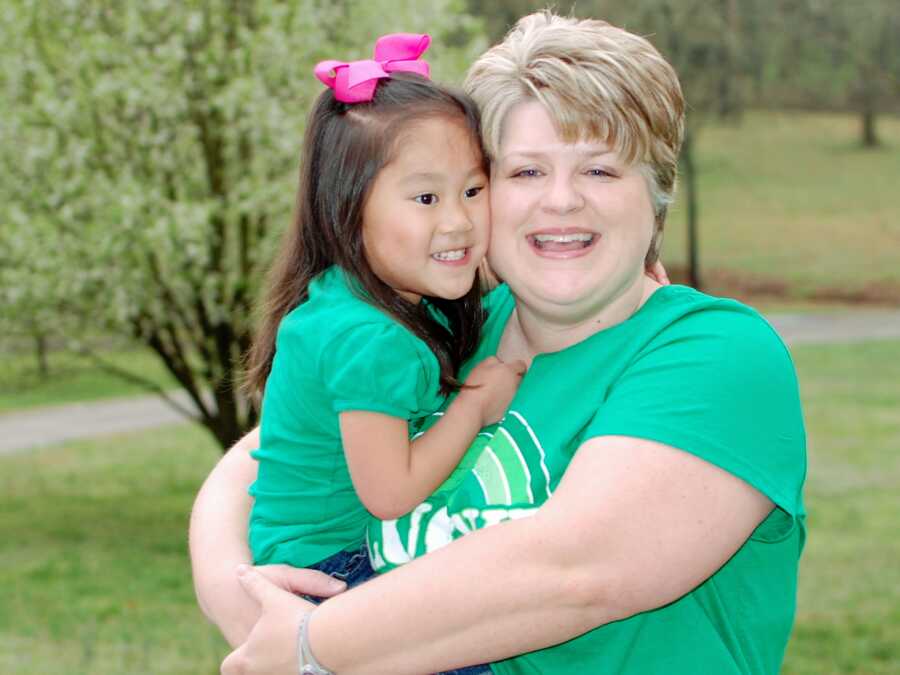 Single adoptive mom holds daughter for picture in matching green shirts.