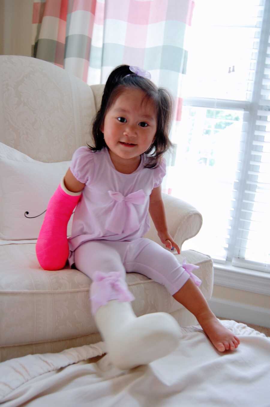 Small Chinese girl takes picture with casts on her hand and foot after surgery.