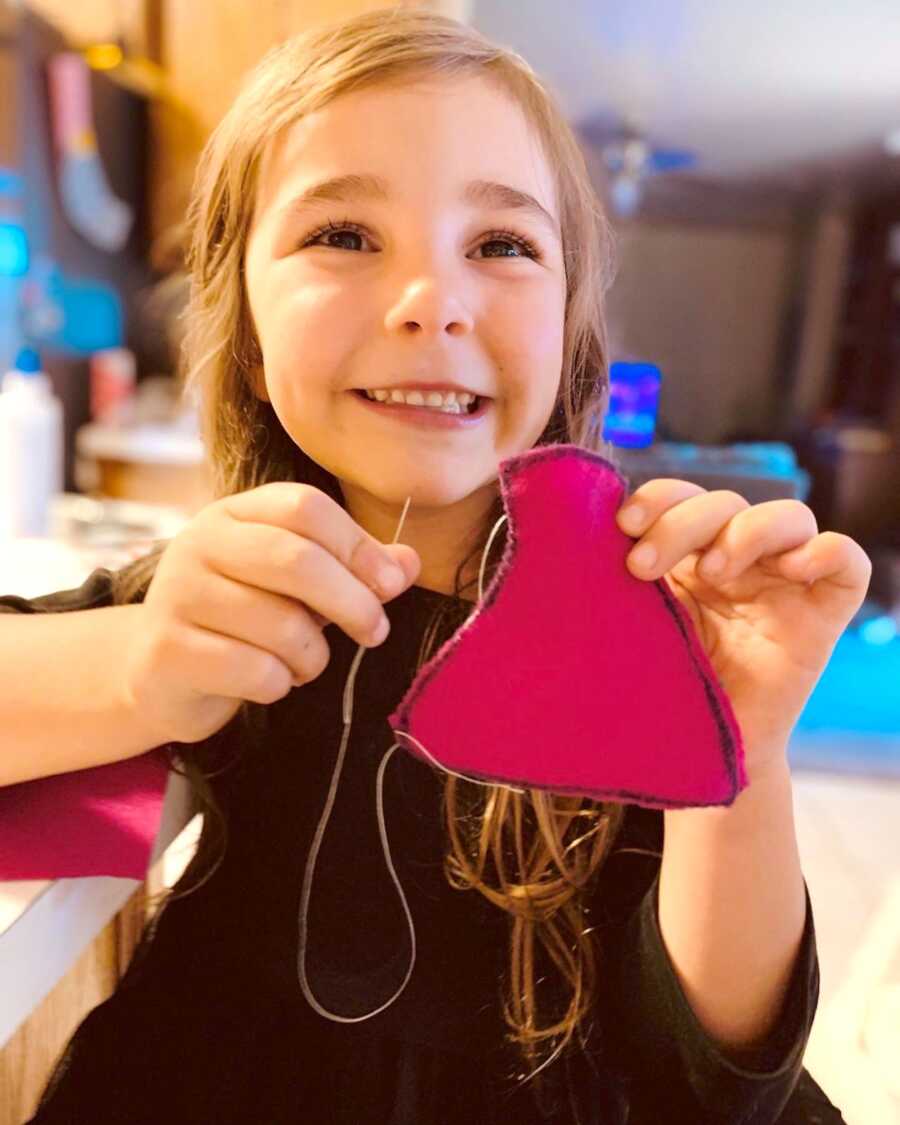 daughter shows her sewing project off to the camera with a large smile on her face