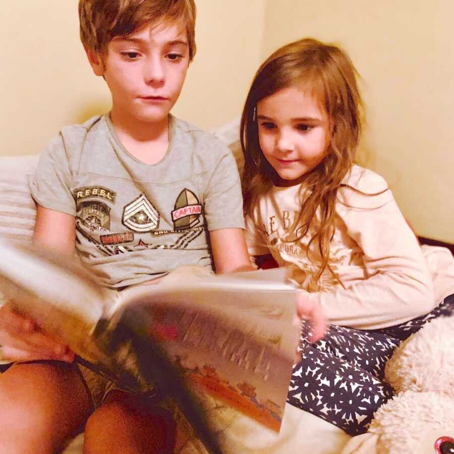 sister sits with her special needs brother as they are flipping through a book