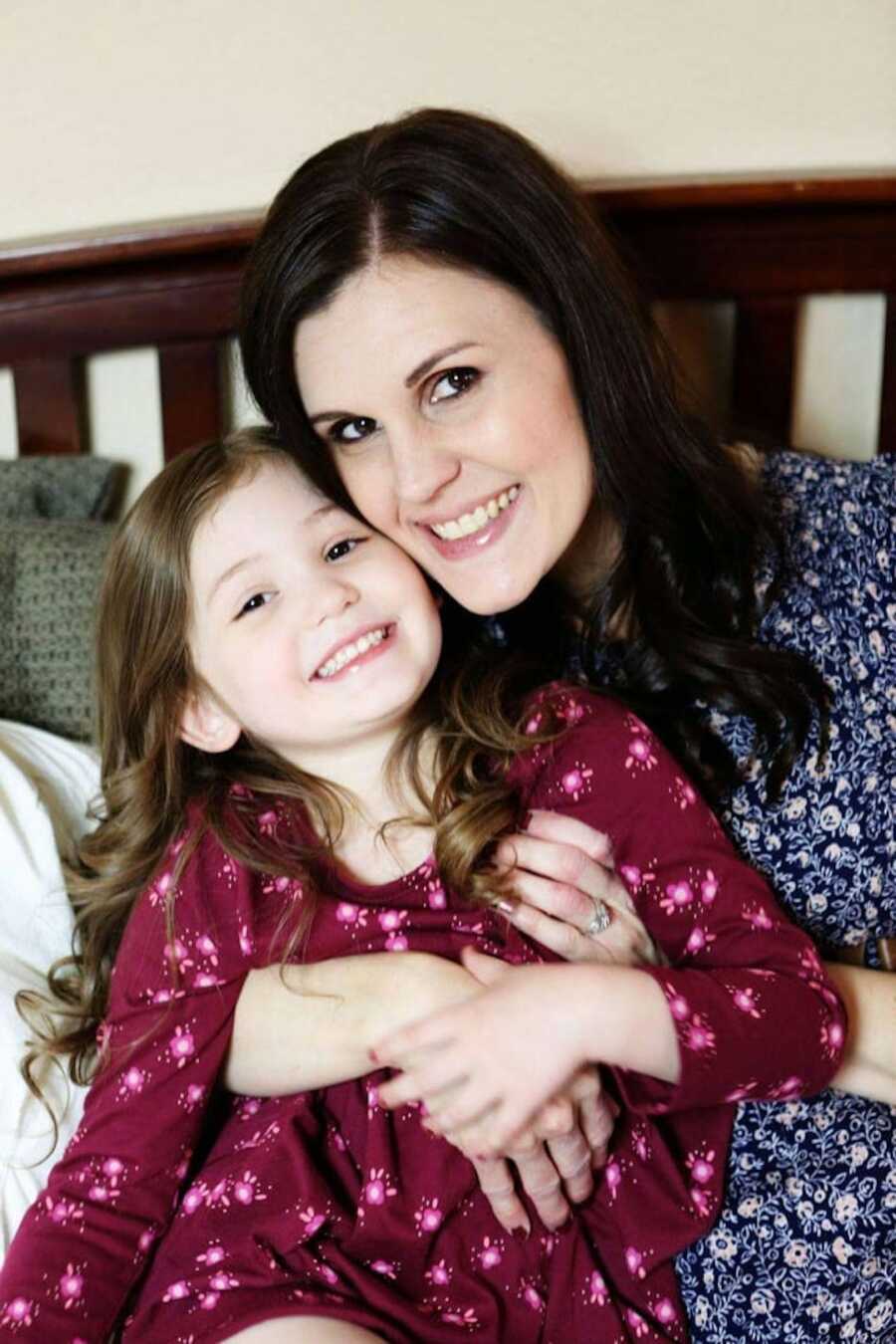 mom holds her daughter close to her while both of them are smiling