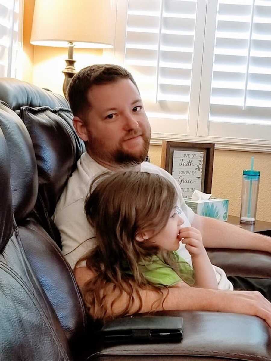 dad sits on the couch with his daughter in his arms next to him