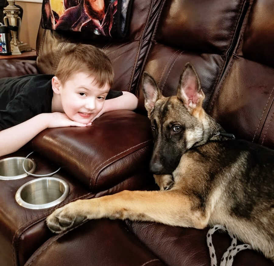 boy with Duchenne's sits on the couch with his german shepherd