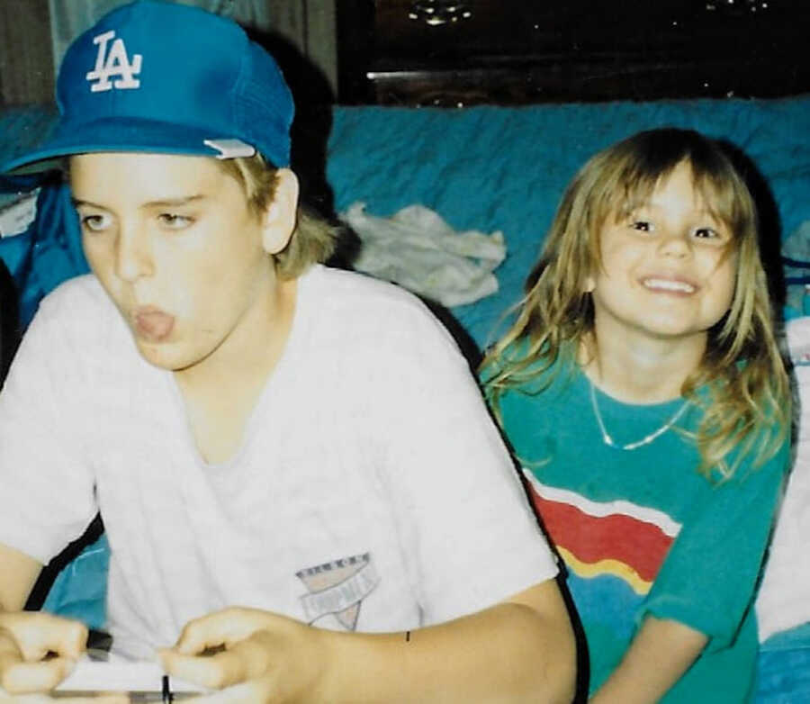 brother and sister spending time together; brother is playing video games while sister smiles