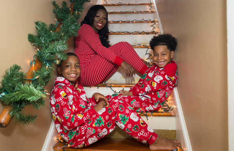 Single mom and sons take picture waiting on stairs in Christmas pajamas.