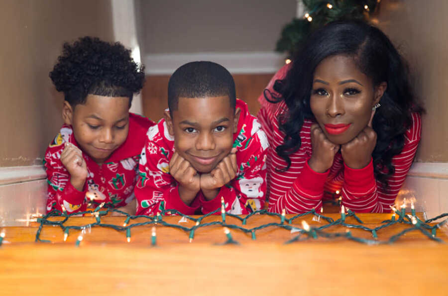 Single mom and boys take picture in pajamas with Christmas lights.