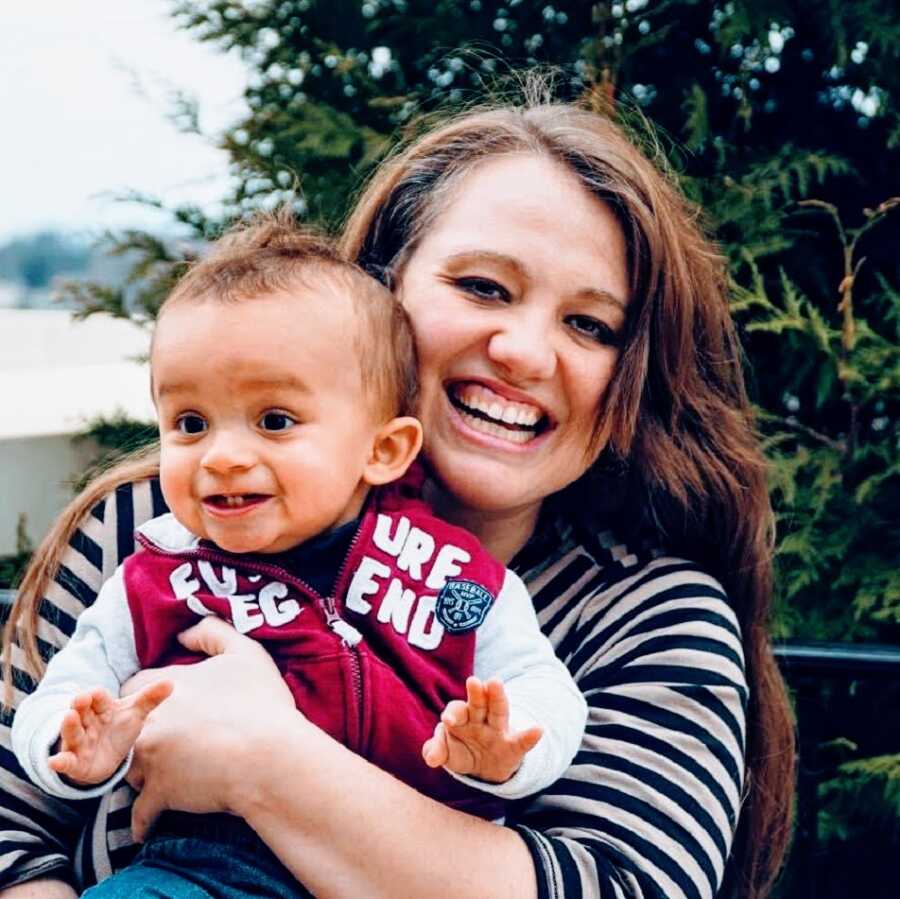 A single mom wearing a striped shirt holds her young son in a chair outside