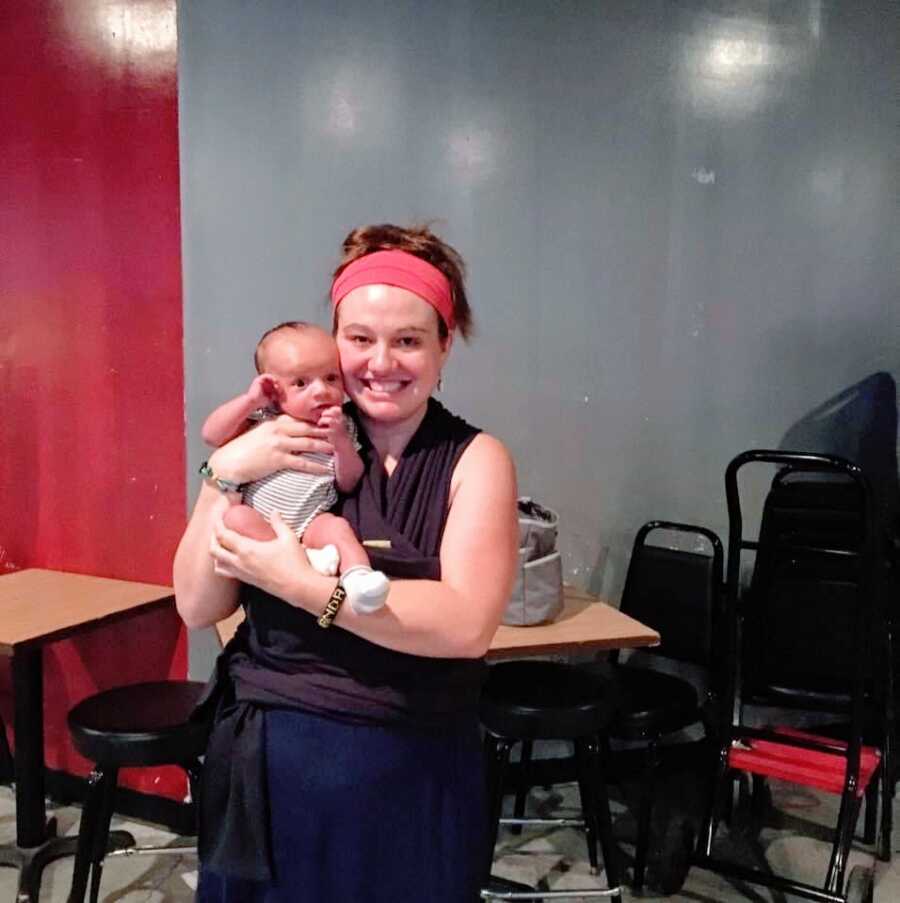 A proud single mom holds her newborn in a grey room filled with black chairs