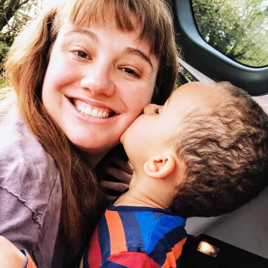 A little boy wearing a colorful striped shirt kisses his mom on the cheek
