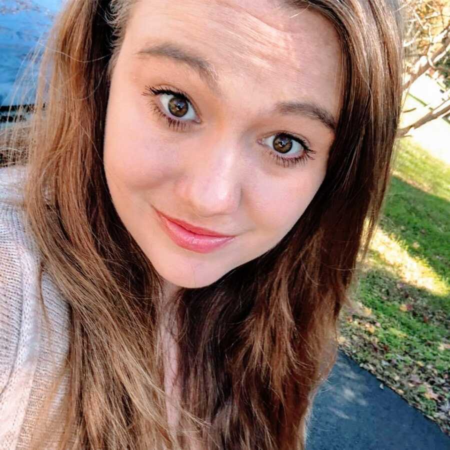 A young woman with brown hair and brown eyes standing outside