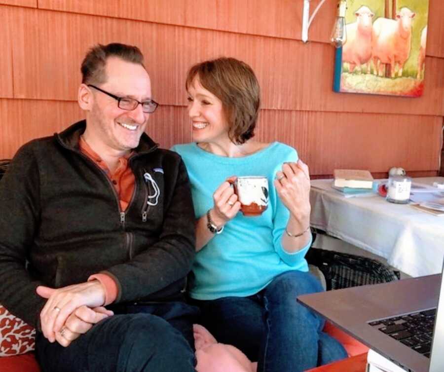 husband and wife sit next to each other in front of a laptop, smiling