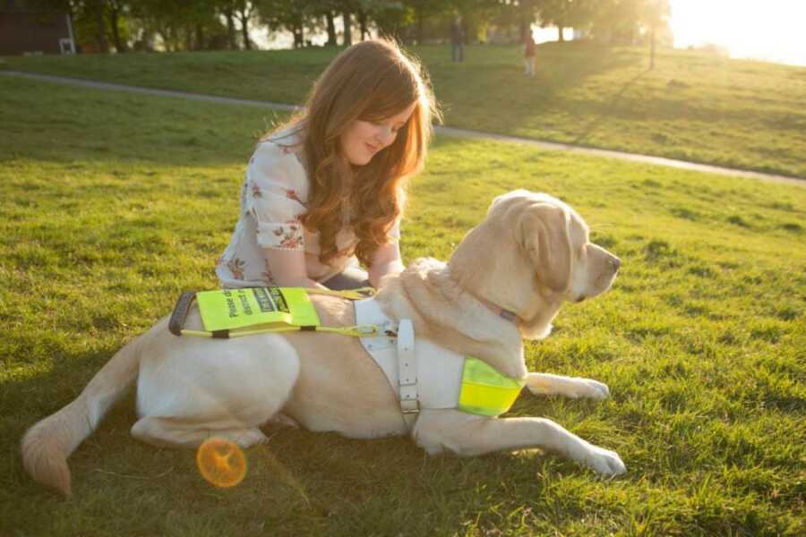 woman sitting in the grass with her guide dog