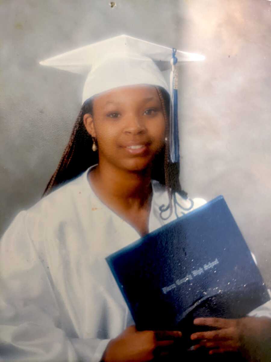 young girl sits for her high school graduation photo with a diploma in her cap and gown