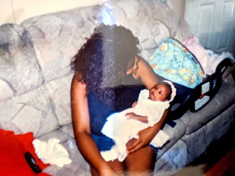 teen mom sits on couch with her daughter on her lap looking down at her