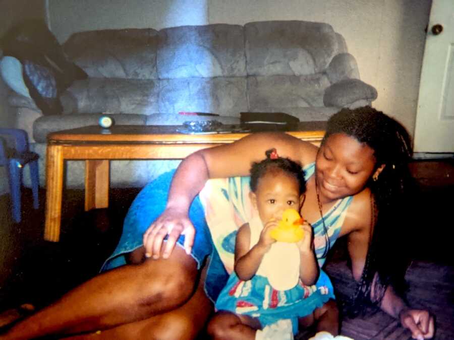 teen mom lays on her side with her daughter sitting in front of her playing with toys