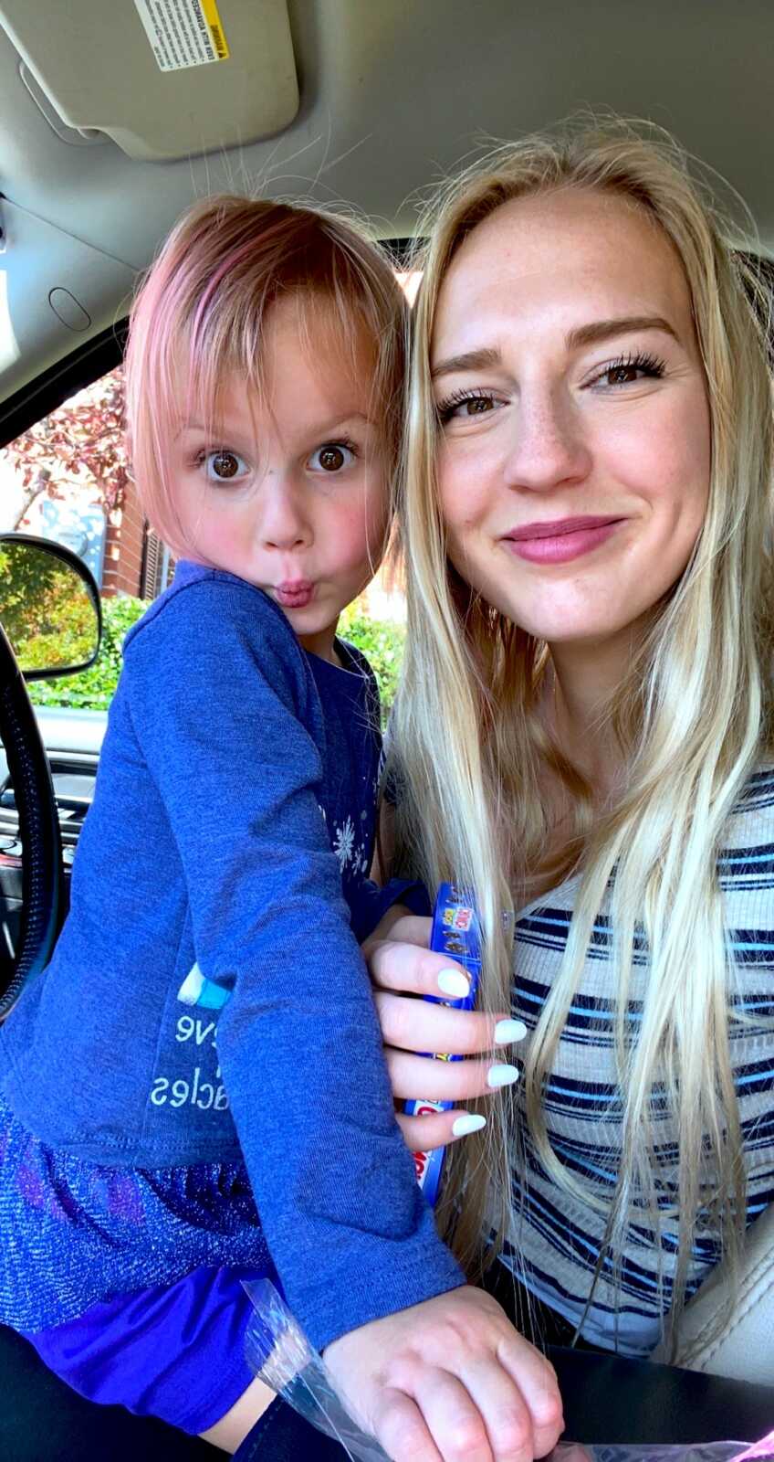 mom takes a selfie in the car with her daughter while the young girl makes a silly face