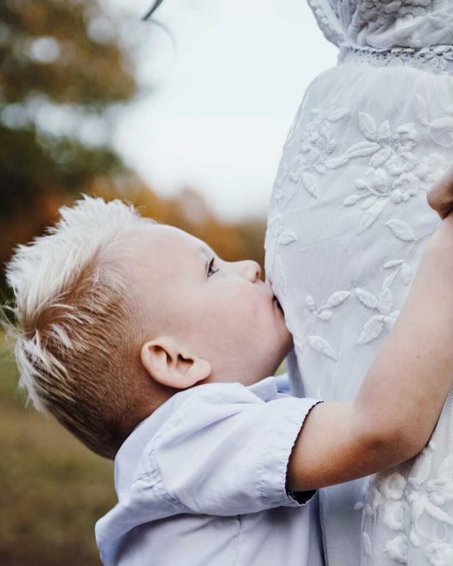 Youngest son kisses mom's pregnant belly in cute family photo.