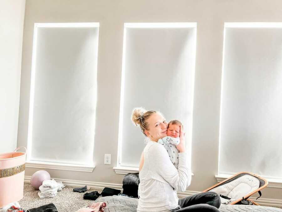 Mom sits alone in bedroom holding brand new baby to her chest. 