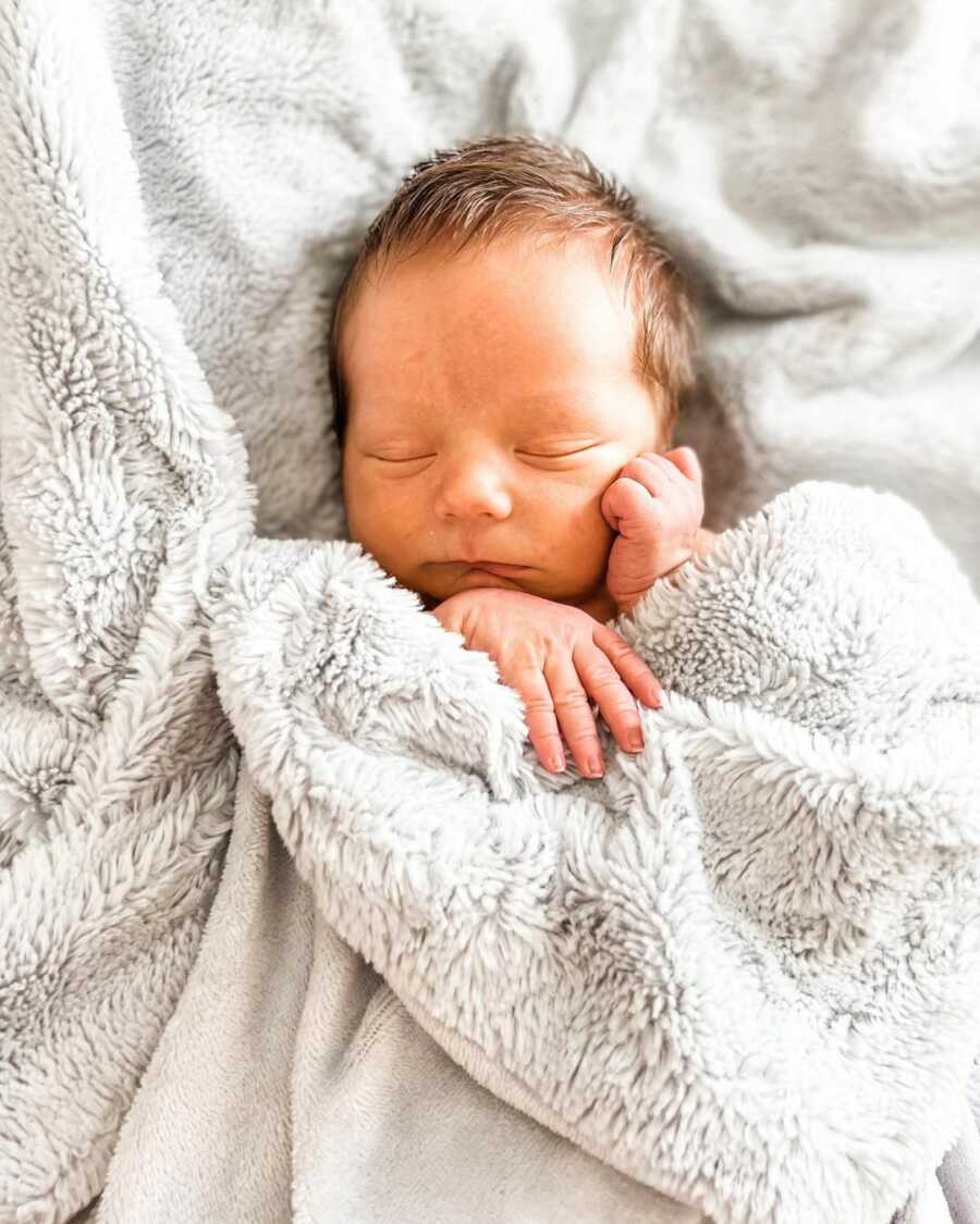 Newborn baby boy wrapped in fuzzy gray blanket.