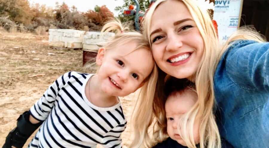 mom poses with her two children in a field taking a selfie, they are smiling