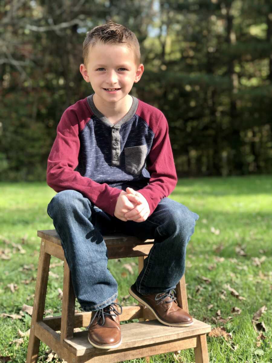 young boy with anxiety poses for a photo outside sitting on a stool