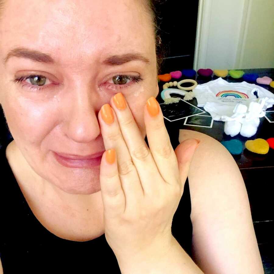 woman pregnant after loss cries with hand to her face with her pregnancy announcement behind her