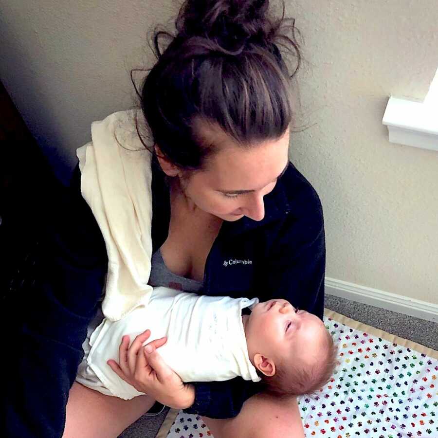 mother of newborn sits on the floor exhausted holding her baby