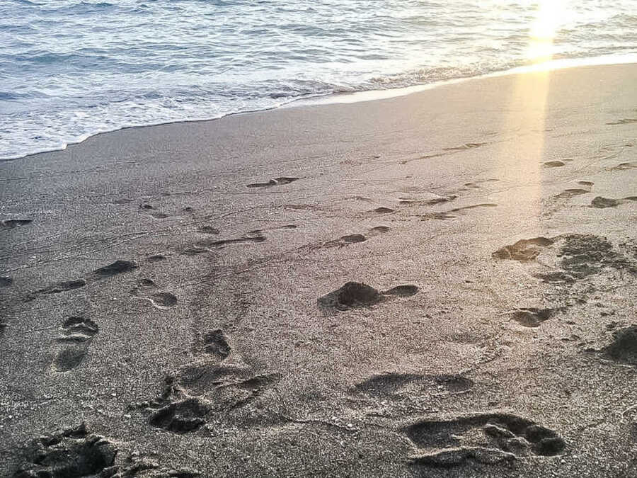 close up of the sand with footprints and a wave coming in
