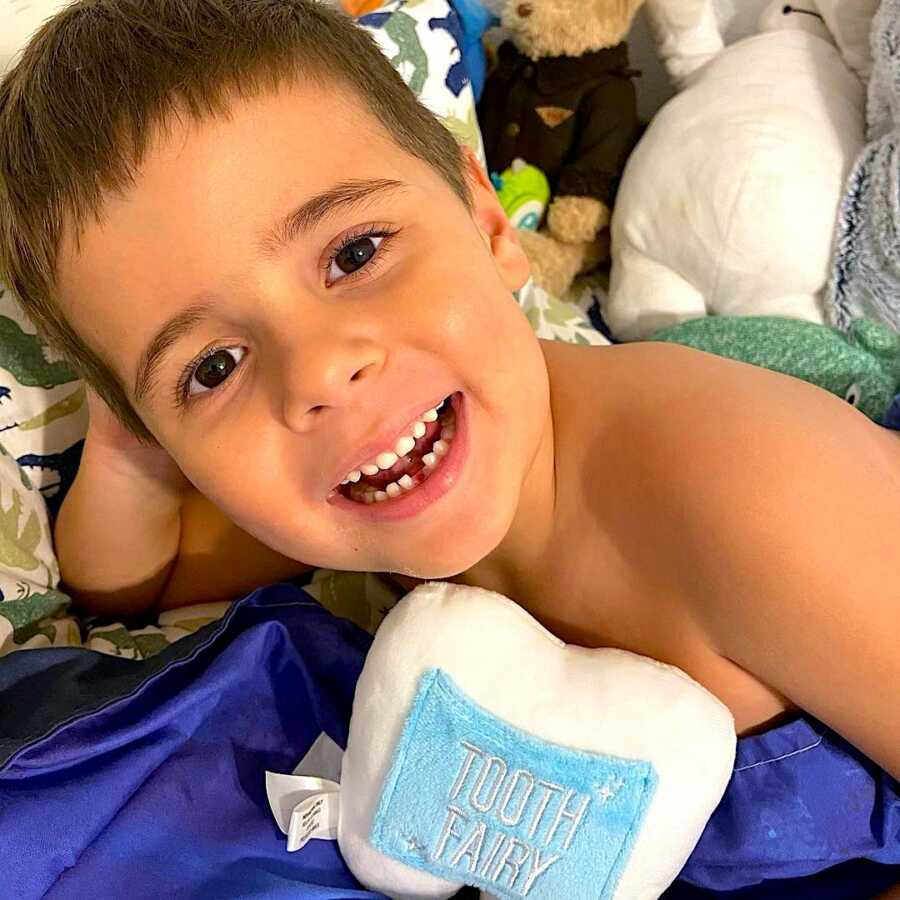 Young boy poses with a missing tooth and a tooth fairy pillow