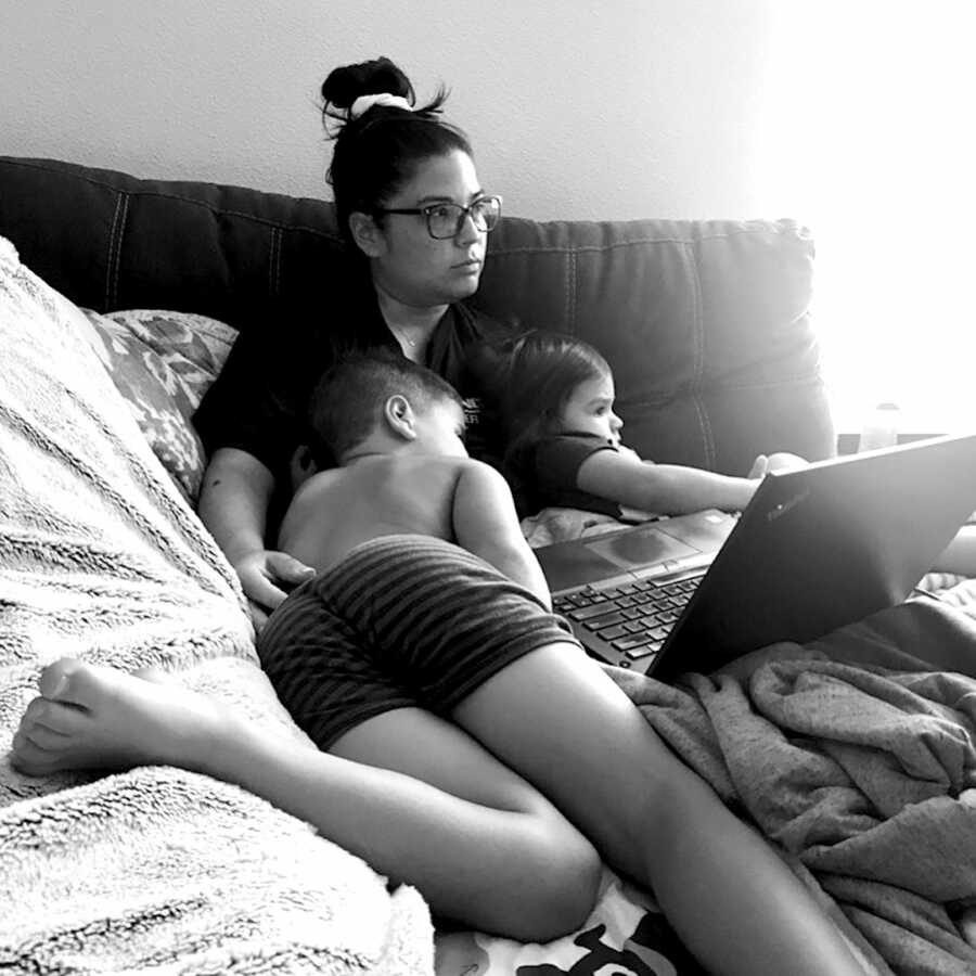 mom sits in bed with her two children resting on her with a laptop on her lap