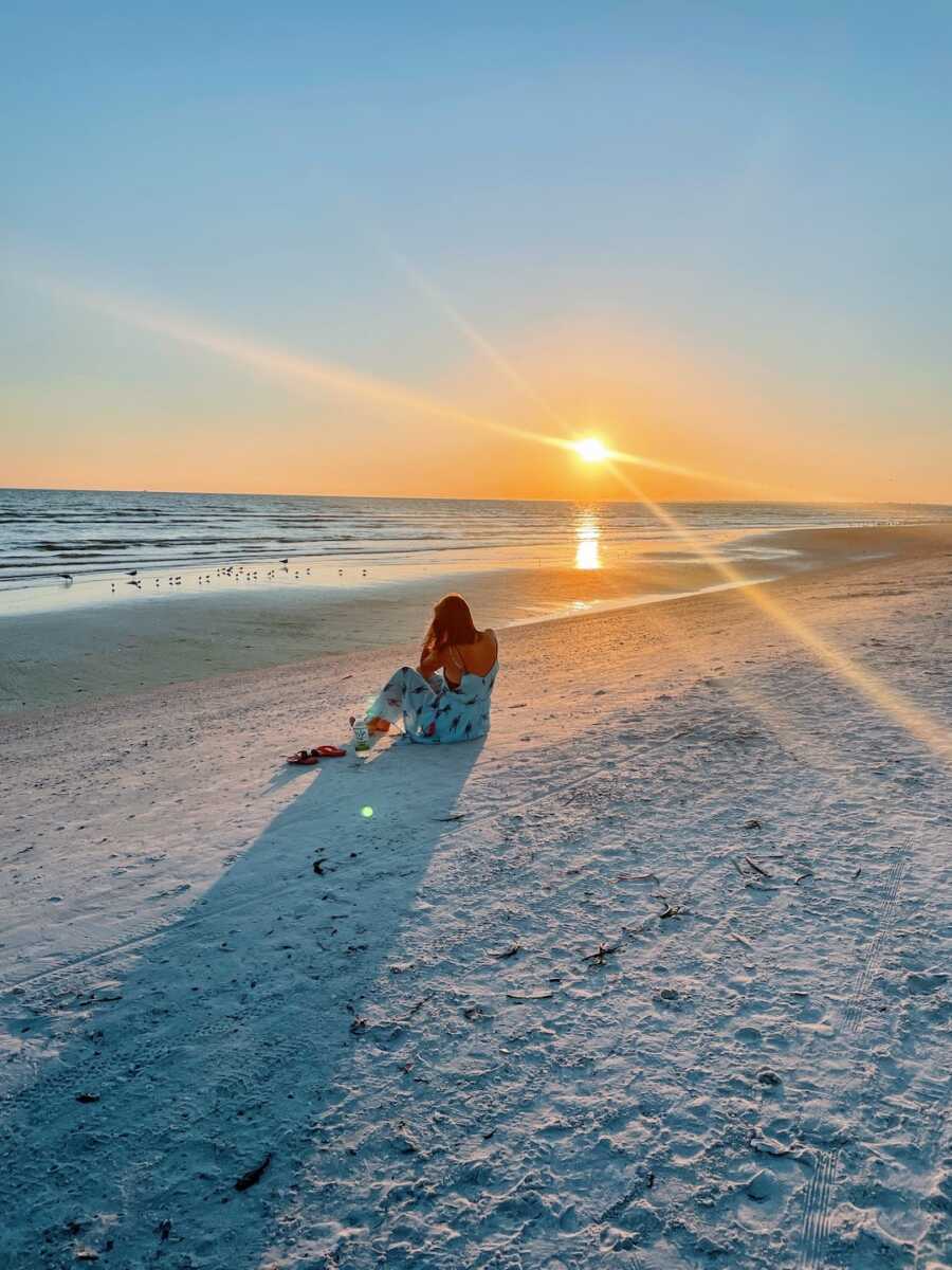 Woman sits alone on the beach at sunset. 