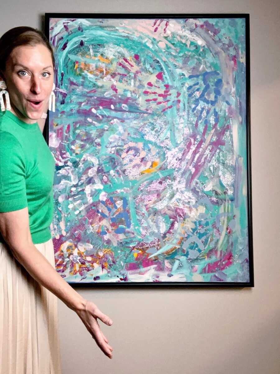 woman poses with one of her paintings created after finding a love for art