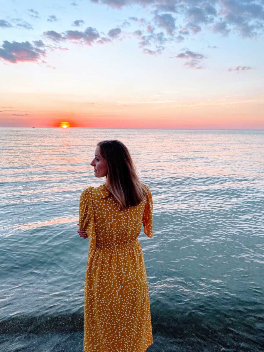woman looks out at the ocean during sunset with her head turned over her shoulder