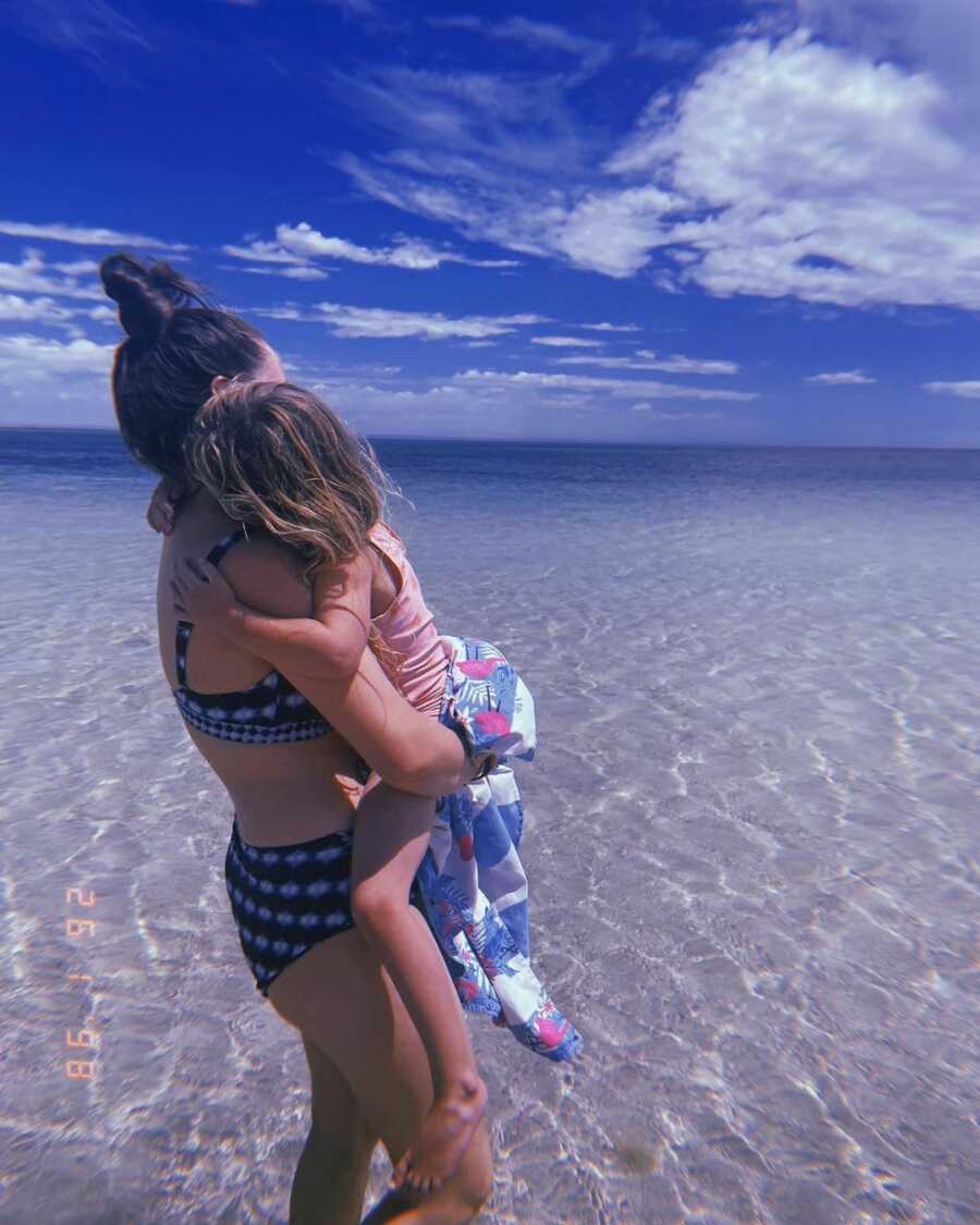 Mother holds her daughter while in the ocean at the beach