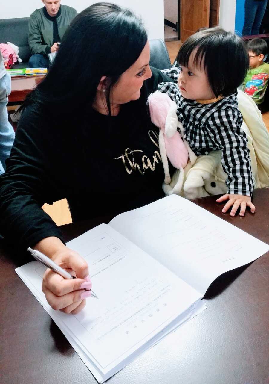 adoptive mother looks at daughter while she is signing paperwork to complete the international adoption
