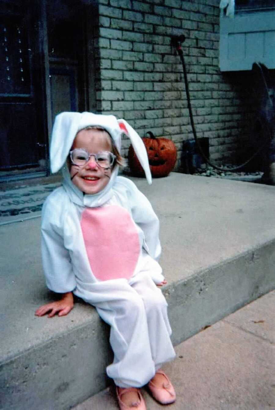 Little girl with unknown chronic illnesses sits on her porch dressed in a bunny costume for Halloween