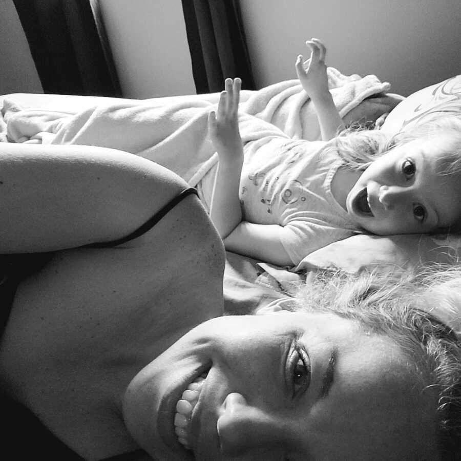 mother lays in bed with her daughter both are smiling