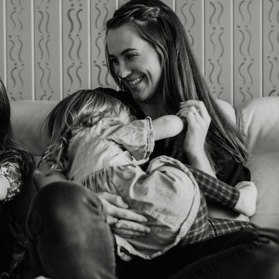 mom sits with her daughter on her lap on a couch, they are laughing together