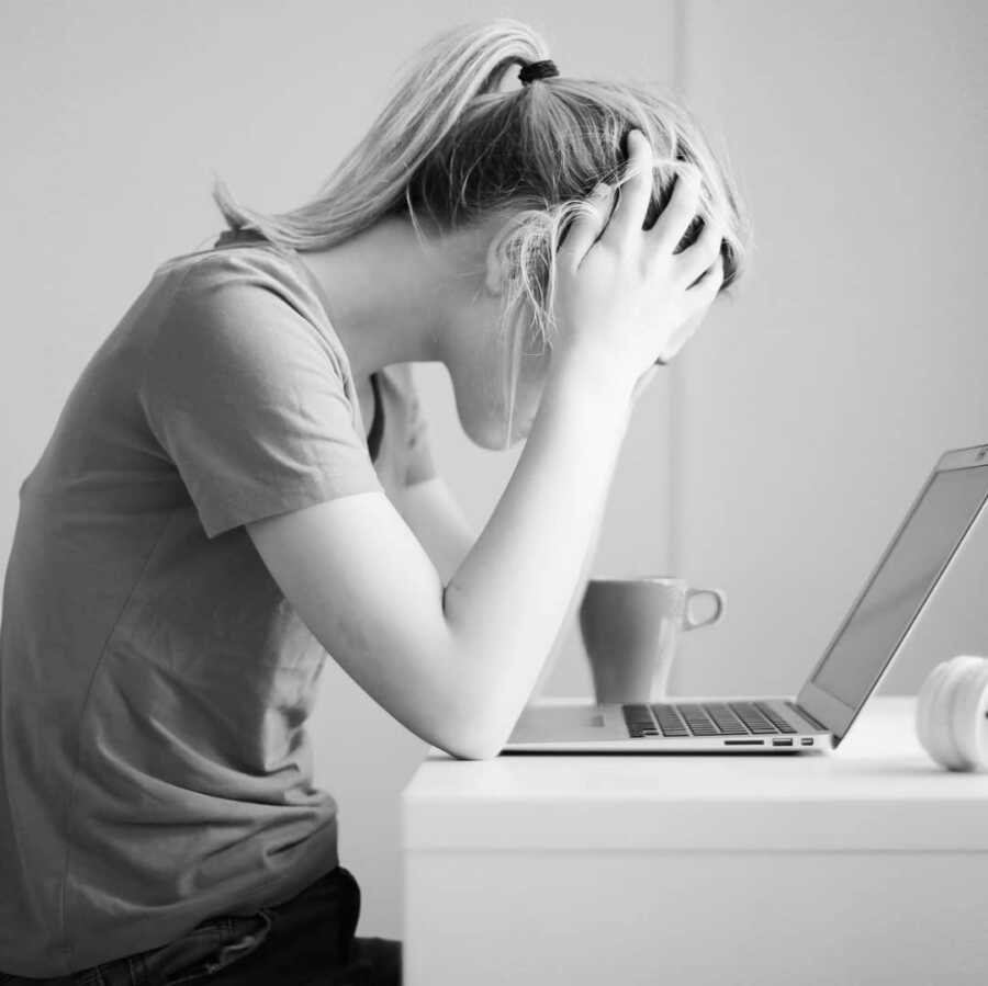 mom looks stressed while looking at computer completing work, hands resting on her forehead