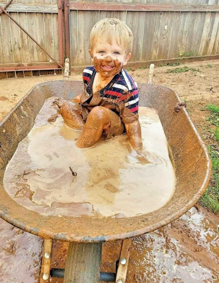 little boy in a wheel barrel full of dirt and mud