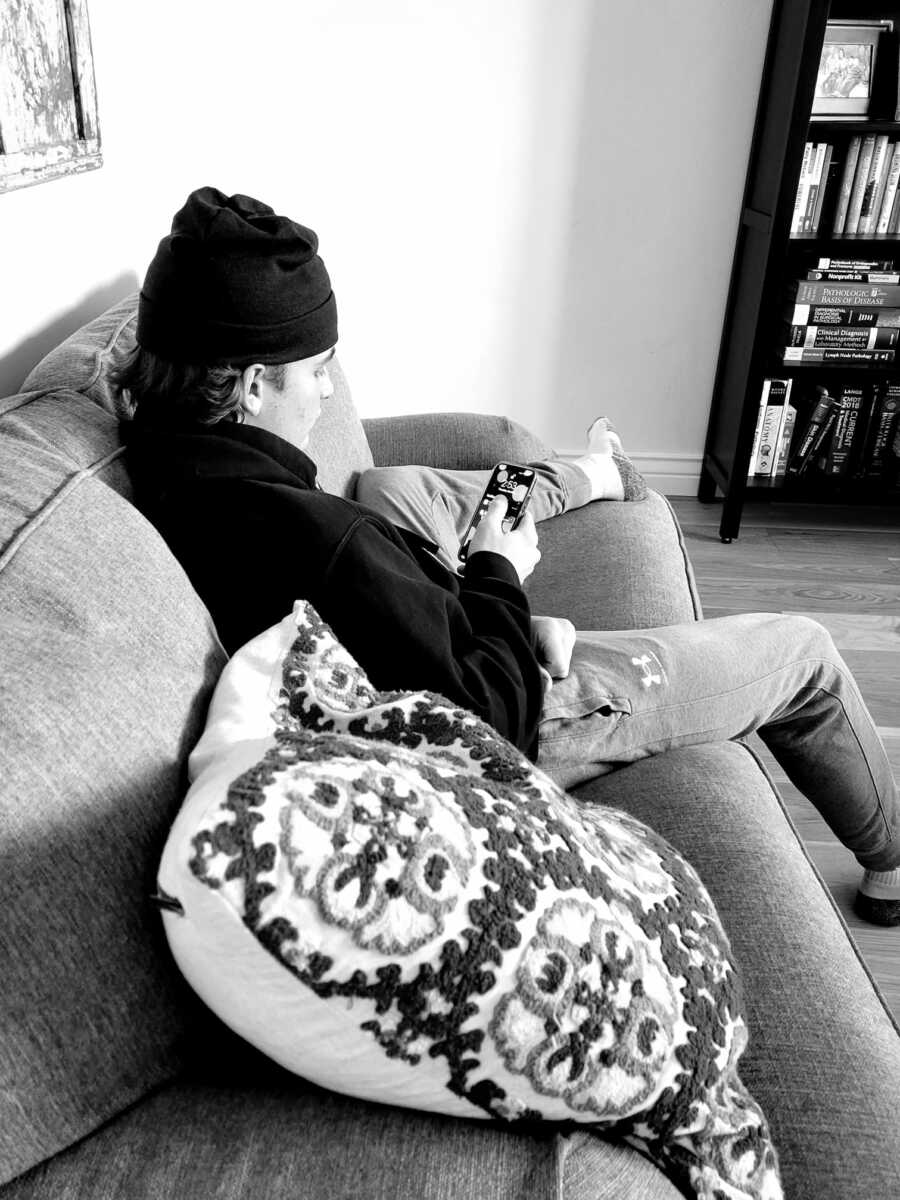 teen boy in a beanie sitting on his phone on the couch