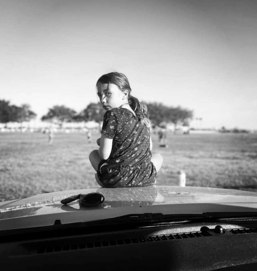 little girl on top of a car looking at mom