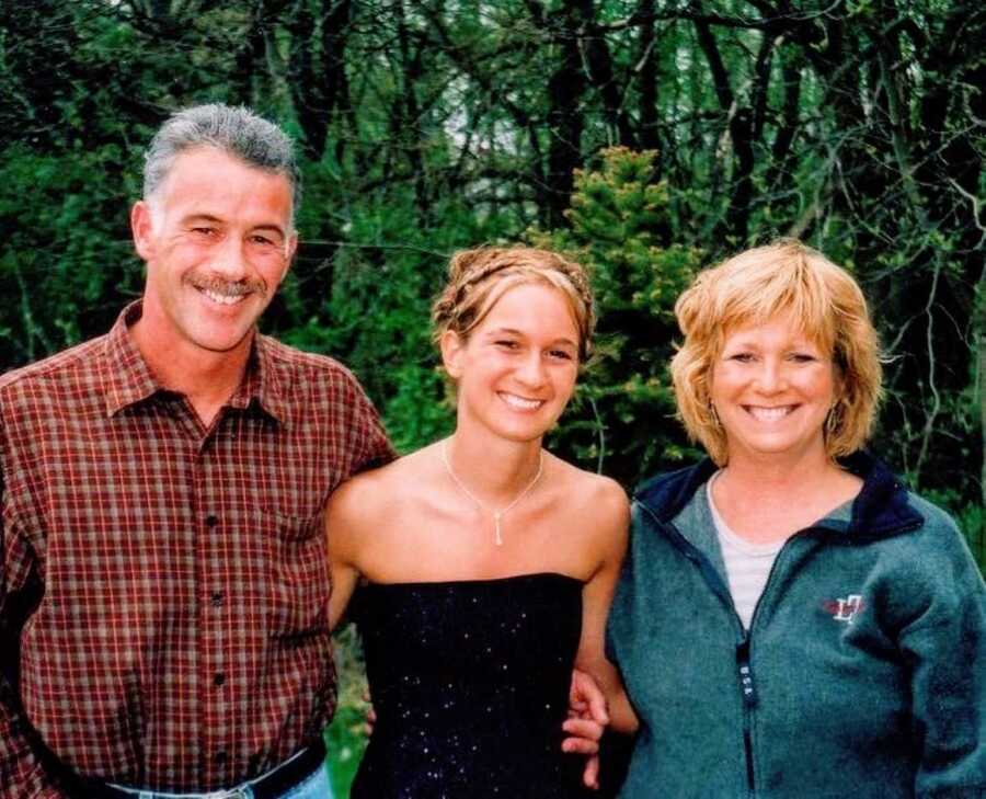 Young woman takes a photo with her parents before going to a dance while wearing a black dress