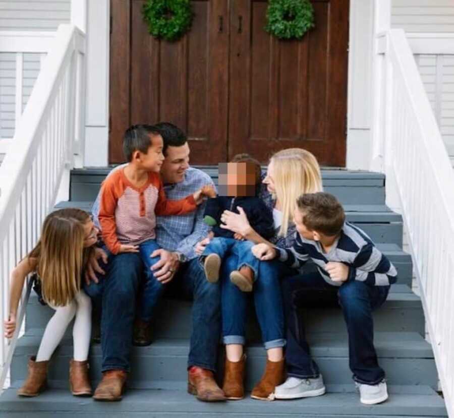 Family of six take a candid photo while they all look at and admire their young foster son